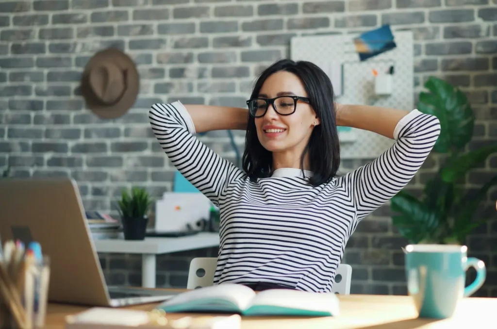 woman at her desk, hands behind her head, smile on her face, looking at a computer screen
